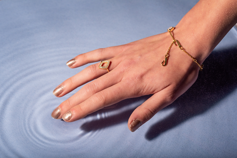 A woman's hand with gold jewelry touching the water