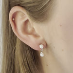 A video of a model wearing Juraster’s Sterling Silver Akoya Pearl Earring Charm, Beachcomber, crafted from Fairmined sterling silver and a responsibly-farmed pearl, attached to a matching sterling silver pearl stud, along with a white gold diamond stud in her cartilage.