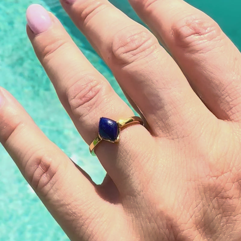 Lodestone gold ring with lapis lazuli, on a hand near a swimming pool